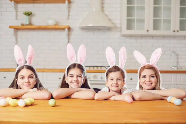 Glad påsk. Mor och döttrar med kaninöron dekorerar påskägg vid ett bord i köket. — Stockfoto