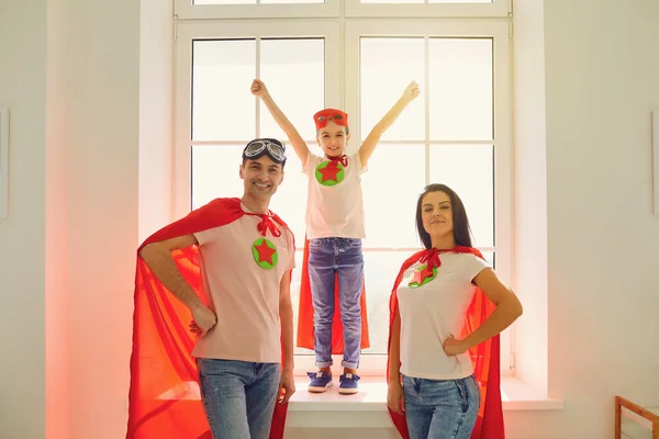 Süper kahramanların kostümleri içinde neşeli bir aile. İçerideki bir odanın arka planında dikilirken gülüyorlar.. — Stok fotoğraf