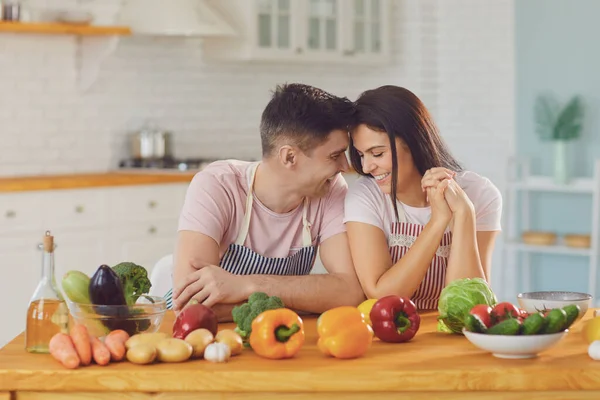 Feliz casal do meio sorrindo a uma mesa com legumes frescos fazer salada na cozinha . — Fotografia de Stock