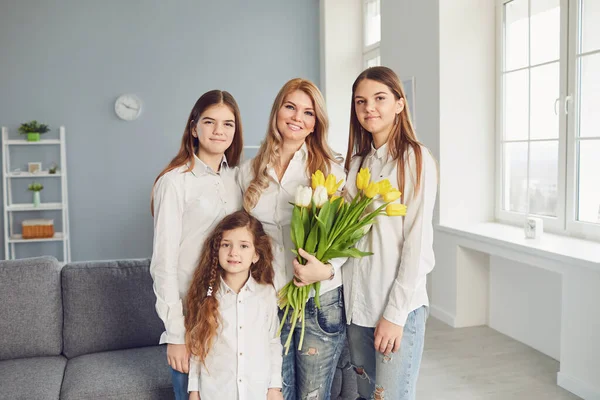 Ευτυχισμένη μέρα μητέρων. Μια μητέρα και τρεις κόρες με λουλούδια σε ένα σύγχρονο σπίτι. — Φωτογραφία Αρχείου