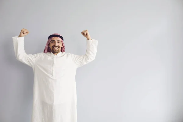 Арабский бизнесмен поднял руки, улыбаясь стоя на сером фоне. — стоковое фото