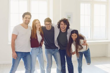 Bir grup neşeli genç, pencereli bir odada dikilirken gülüyor..