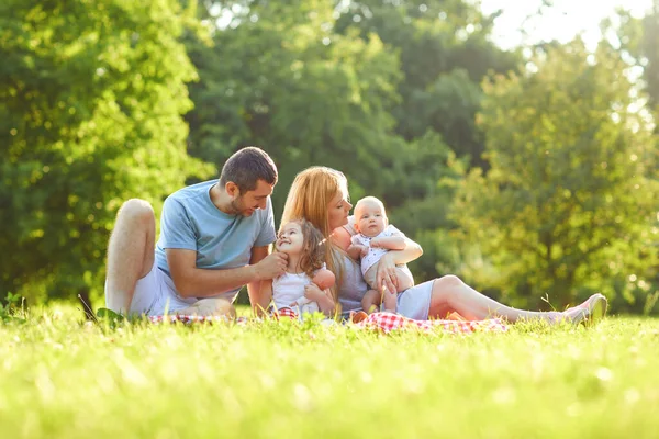 Lycklig familj sitter på det gröna gräset leker i parken. — Stockfoto