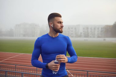 Spor giyimli bir adam antrenmandan sonra stadyumda oturuyor..