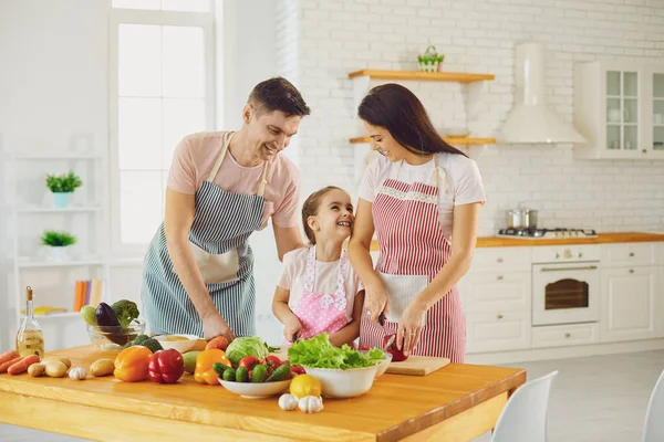 Família feliz com criança preparando legumes frescos na mesa na cozinha . — Fotografia de Stock