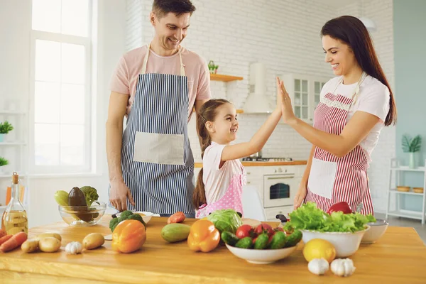 Família feliz com criança preparando legumes frescos na mesa na cozinha . — Fotografia de Stock