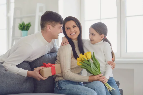 Gelukkige Moederdag. Vader en baby dochter feliciteert moeder met bloemen en een ansichtkaart in een kamer — Stockfoto