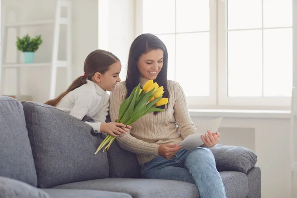 Hari ibu bahagia. Putri selamat memeluk ibunya memegang karangan bunga di dalam ruangan.. — Stok Foto