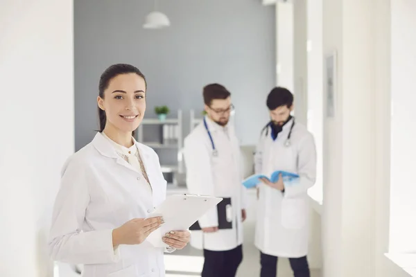 Un médico varón con un estetoscopio sonriendo un portapapeles mientras está de pie en una clínica . —  Fotos de Stock