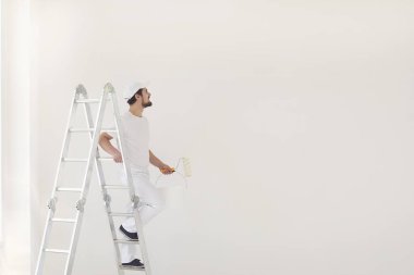 Beyaz üniformalı bir erkek ressam elinde bigudiyle beyaz bir odada çalışıyor.