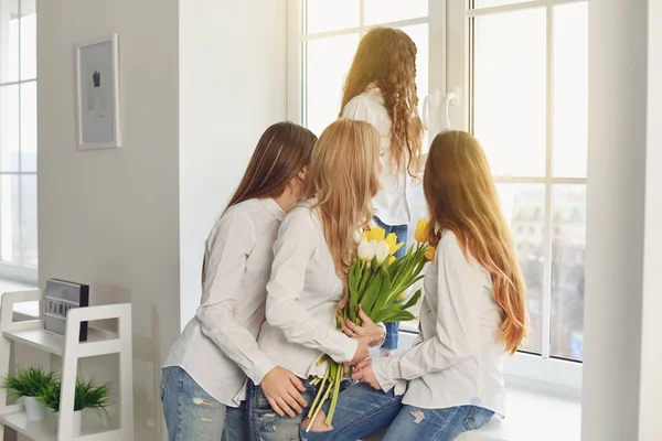 어머니 날 축하 해. 집안 창문을 들여다보고 있는 꽃을 든 어머니와 세 딸. — 스톡 사진