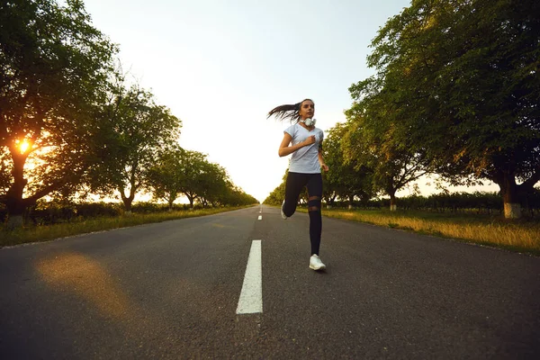 Девушка-бегунья бежит по дороге на рассвете — стоковое фото