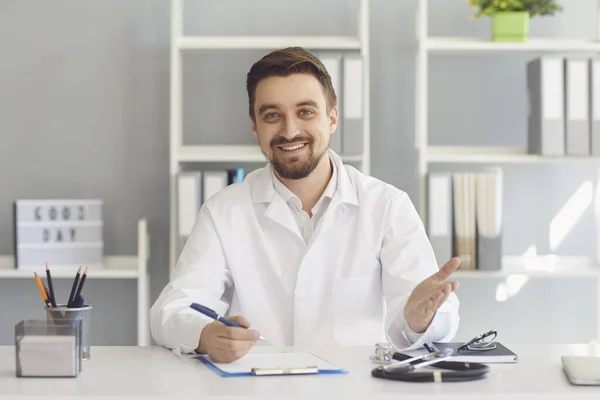 Smiling female doctor gives consultation at a table in a clinic office.