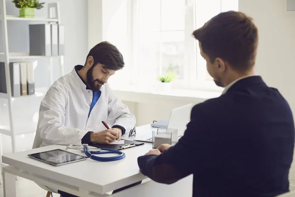 Patient beim Arztbesuch in der Klinik. Ärztliche Arbeit schreibt ein Rezept auf einen Tisch im Krankenhaus. — Stockfoto