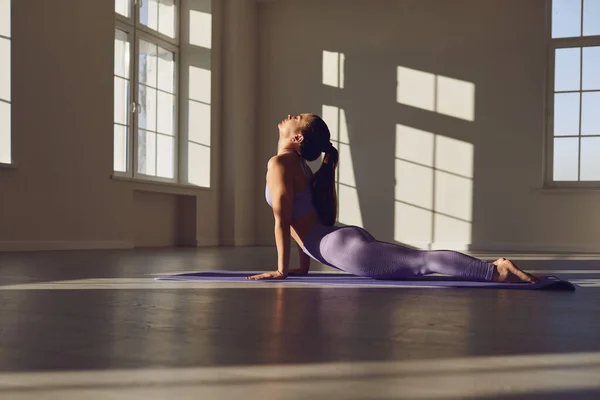 Yoga sınıfındaki yogacı kadın güneşli pencereli bir odada yerde yoga yapıyor.. — Stok fotoğraf