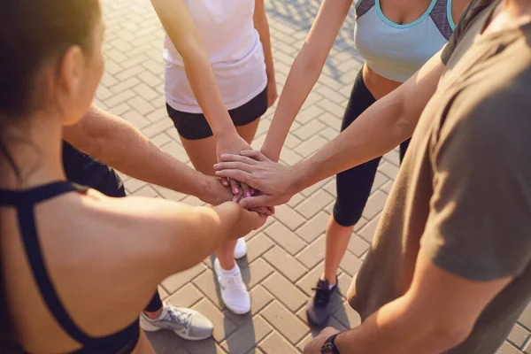 Group of sporting people join hands in the park at training.