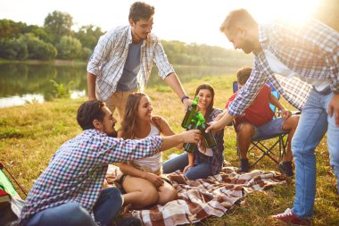 Young people drink, eat and clink glasses at a picnic