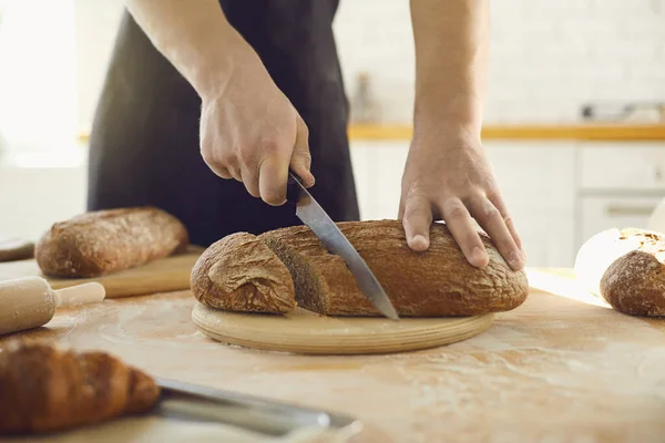 Руки, що ріжуть свіжий домашній хліб на столі на кухонній пекарні . — стокове фото