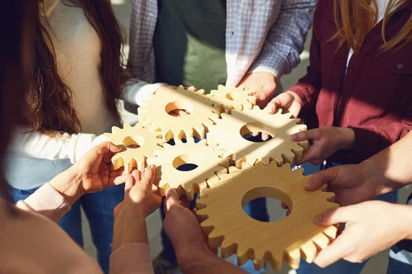 Eine Gruppe junger Geschäftsleute in Freizeitkleidung hält hölzerne Zahnräder in den Händen.. — Stockfoto