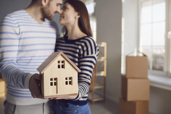 Szczęśliwa para trzyma model domu w rękach nowego domu mieszkanie pokój. — Zdjęcie stockowe