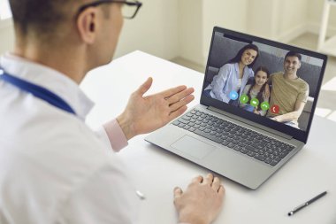 Aile doktoru hatta. Erkek doktor, klinikte saman başında dizüstü bilgisayar kullanarak hastalarla konuşur..
