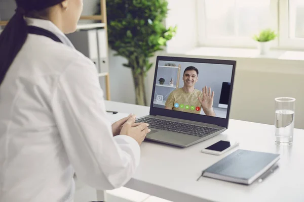 Female doctor online. Doctor speaks with a patient using a laptop sitting behind a straw in a clinic office. Online medical consultation. — Stock Photo, Image