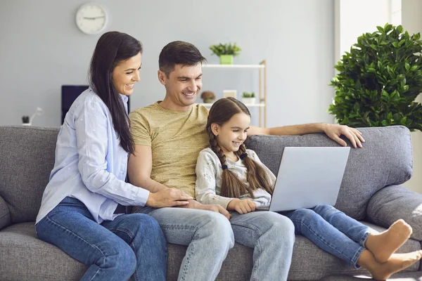 Feliz família conversando on-line usando laptop enquanto está sentado com o bebê no sofá em casa . — Fotografia de Stock