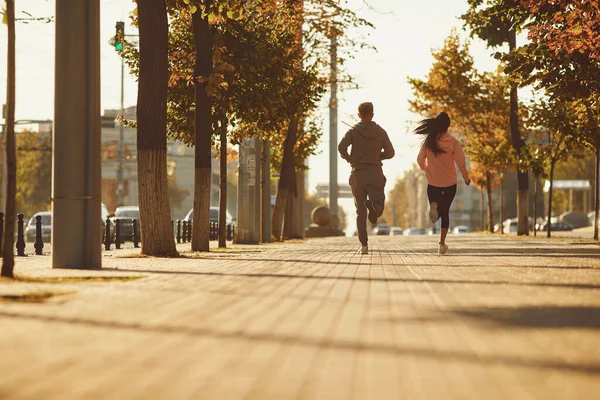 Un uomo e una donna stanno correndo lungo la strada della città la mattina . — Foto Stock