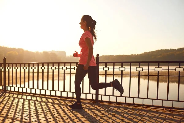 Girl runner runs in a park by the lake at dawn — Zdjęcie stockowe