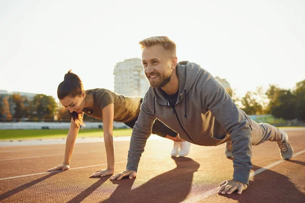 Young couple doing pushups in the stadium — Stock Photo, Image