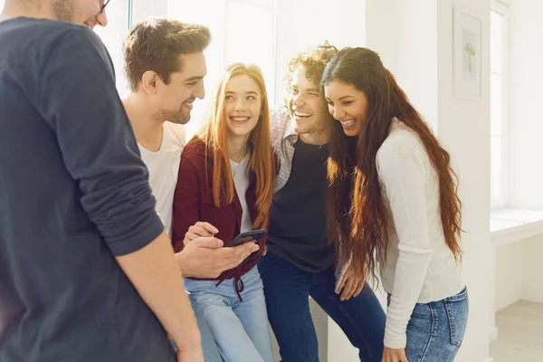 Grupo de amigos felices mirando el teléfono riendo sonriendo en una habitación luminosa . — Foto de Stock