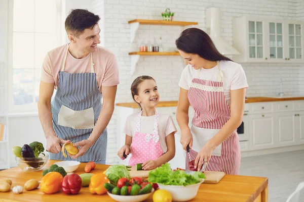 Familia feliz con el niño preparando verduras frescas en la mesa en la cocina . — Foto de Stock