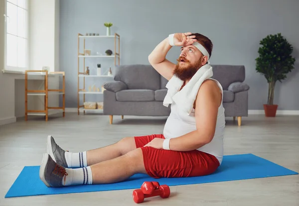 집 바닥에 앉아서 웃으면서 바닥에서 운동하는 빨간 뚱뚱 한 남자. — 스톡 사진