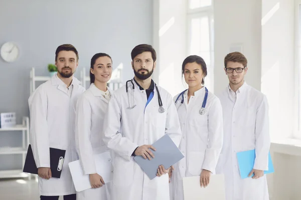 Eine Gruppe selbstbewusst praktizierender Ärzte in weißen Kitteln lächelt vor der Kulisse der Klinik. — Stockfoto
