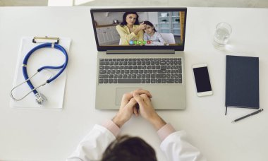 İnternetten çocuk doktorunu ara. Doktor hatta. Terapist, evde oturan bir dizüstü bilgisayarla bir aile annesine ve kızına danışıyor. Üst görünüm.