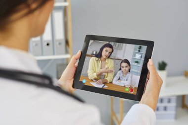 Doktor hatta. Bir kadın doktor terapist, anne ve kızını dinlerken bir tabletin ekranına bakıyor..