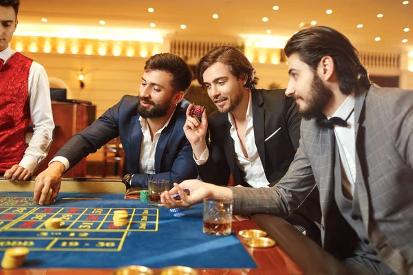 Hombre de grupo jugador en un traje en la ruleta de mesa jugando al póquer en un casino . — Foto de Stock