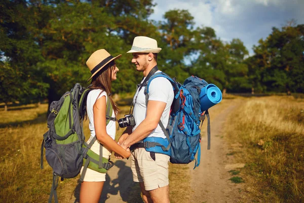 Happy couple of travelers with backpacks hold hands on nature — ストック写真