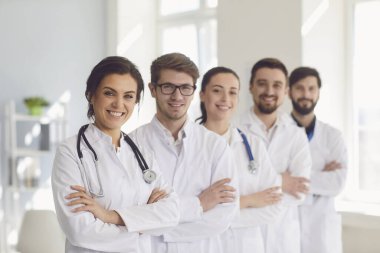 Beyaz önlüklü doktorlardan oluşan bir grup kliniğin arka planına gülümsüyor..
