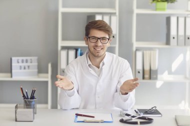 Konsültasyonda çalışan erkek doktor ofiste bir masada otururken konuşuyor..