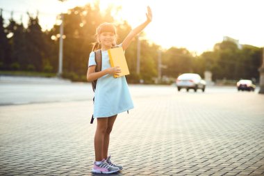 Sırt çantası ve kitapları olan bir kız öğrenci şehir caddesinde duruyor. Okula geri dön.