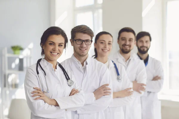 一群身穿白衣、自信的执业医生在诊所的背景下微笑着. — 图库照片