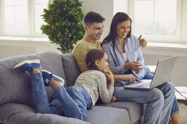 Szczęśliwa rodzina patrząc na laptopa siedząc wygodnie na kanapie w salonie w weekend. — Zdjęcie stockowe