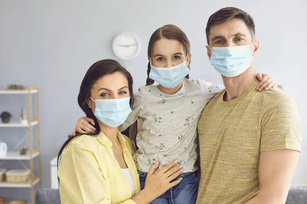 Family in medical masks on the face looks at the camera while standing in the room at home.