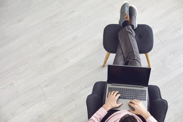 Top view of a man with a laptop sitting in a chair on a gray floor background.