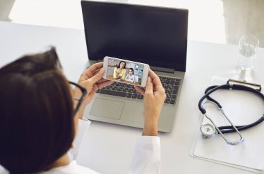 Doktor online tıbbi danışma video görüşmesi. Kadın çocuk doktoru bir kadını ve kızını ateş virüsü belirtileriyle dinliyor..
