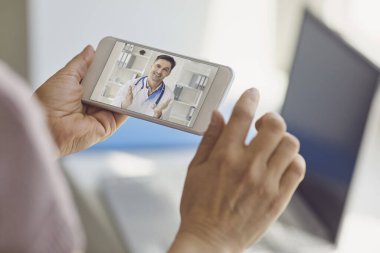 Doktor hatta. Doktor görüntülü sohbet yoluyla danışmanlık yapıyor. Evde oturan cep bilgisayarını kullanıyor..