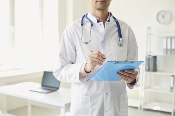 Nahaufnahme eines Arztes schreibt ein Rezept in ein Klemmbrett, um einen Patienten zu behandeln, während er in der Praxis einer medizinischen Klinik steht. — Stockfoto