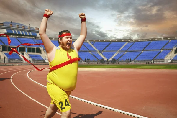 A fat man runs to the finish line on the track.