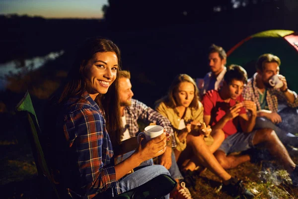 Dívka s hrnkem čaje na pozadí přátel u táboráku v noci — Stock fotografie